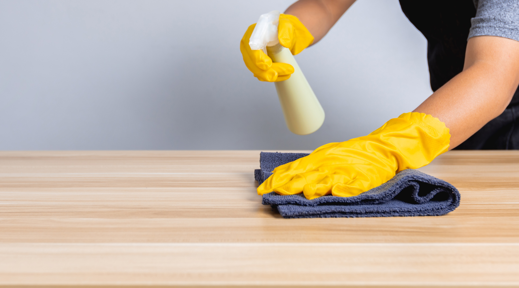 Person holding spray bottle and wiping a medium wood table with the other hand