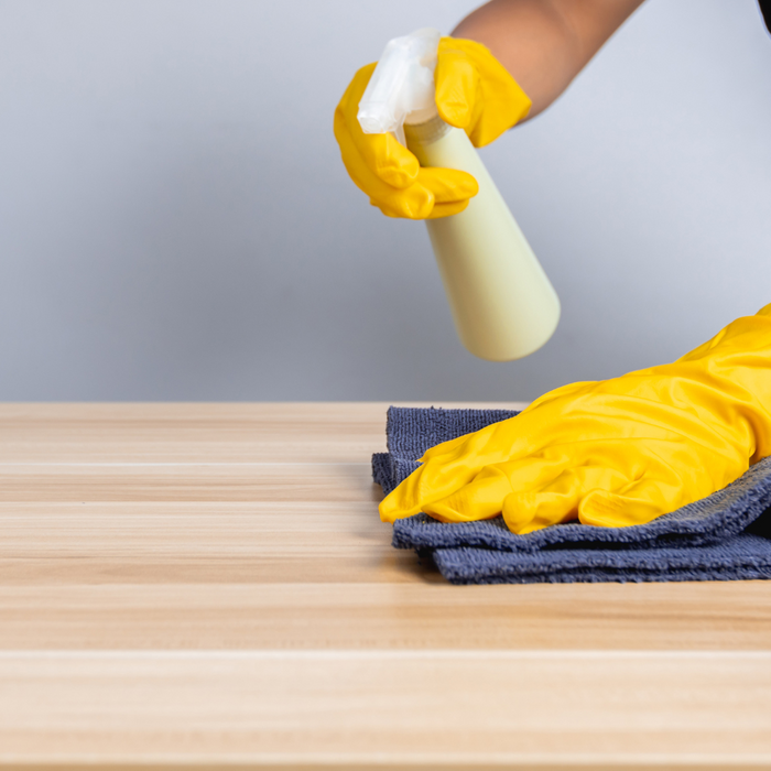 Person holding spray bottle and wiping a medium wood table with the other hand